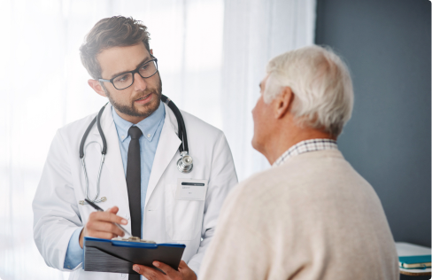 Male doctor holding clipboard talking to elderly male patient.